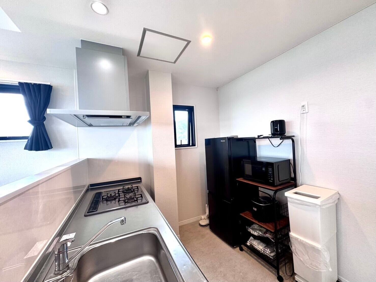 A compact kitchenette with a gas stove, sink, and black microwave on a wooden shelf.