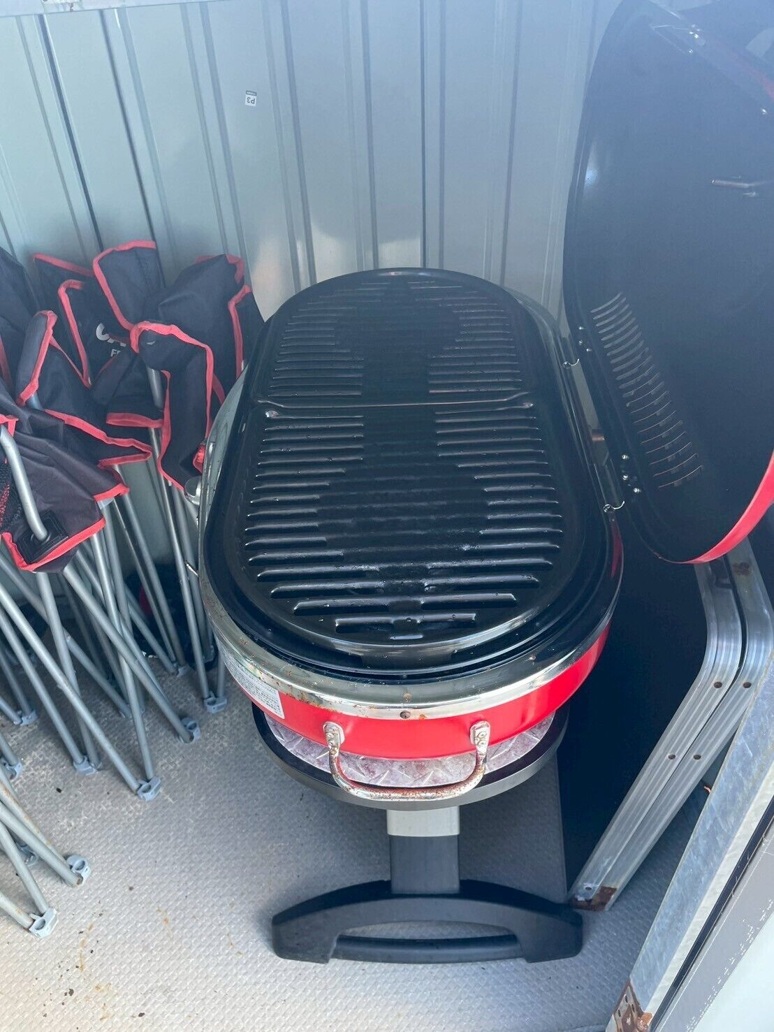 Un barbecue portable doté d’un couvercle noir et de touches de couleur rouge, posé sur une surface texturée.