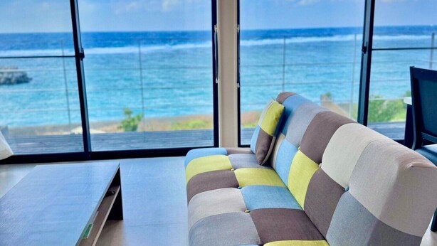 A modern room with a large window overlooking the ocean, a sofa, and a flat-screen TV. - AZ Hotel Ocean View (Amami)