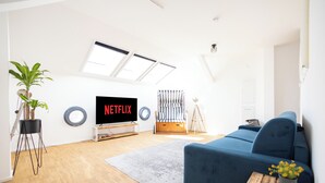 Una sala de estar moderna con un sofá azul, un televisor de pantalla plana mostrando 'NETFLIX', una planta en maceta y una cortina a rayas.