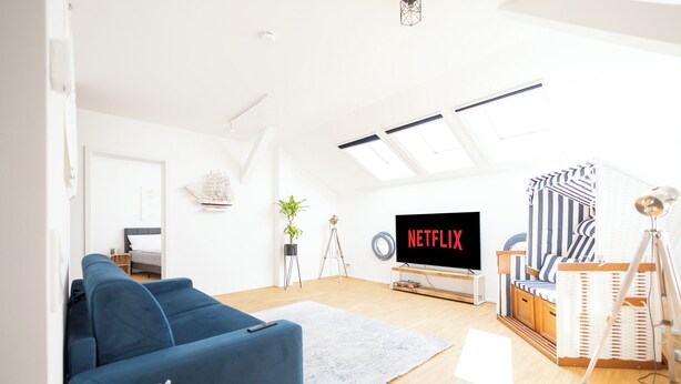 Una sala de estar moderna con un sofá azul, un televisor de pantalla plana, una mesa de centro de madera y una pequeña planta.