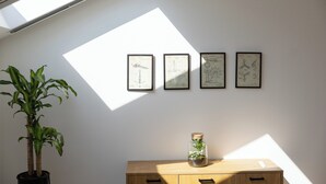 Una habitación con tragaluz, un escritorio de madera, una planta en maceta y cuatro dibujos enmarcados en la pared.