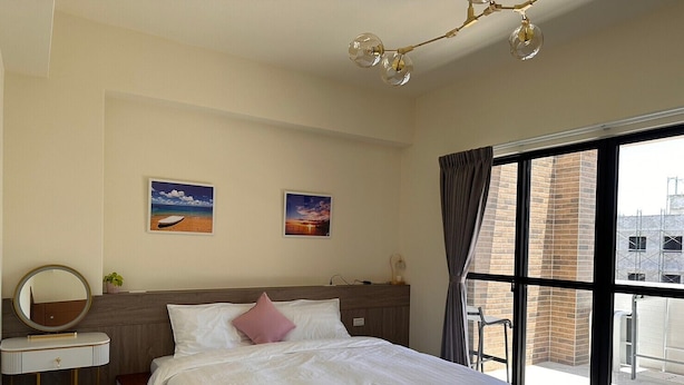 A hotel room with a large bed, a bedside table with a mirror, a small stool, and two framed pictures on the wall. - SeaWave (Magong)