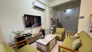 A living room with a flat-screen TV, wooden furniture, a plant, and a kitchen area in the background. - SeaWave (Magong)