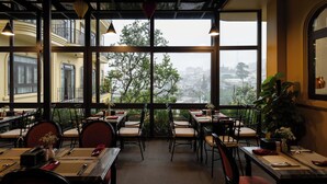 A restaurant with tables and chairs arranged for dining, large windows offering a view of the city, and hanging pendant lights. - Goldient Boutique Hotel (Xuan Huong - Da Lat)