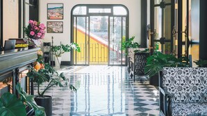 A lobby with a checkered floor, a reception desk, potted plants, and a large window with a view of the outside. - Goldient Boutique Hotel (Xuan Huong - Da Lat)