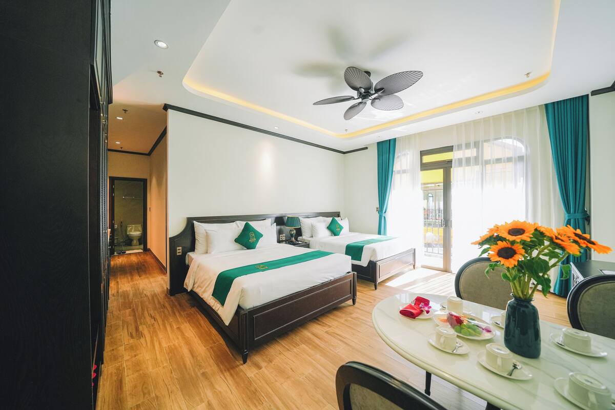 A hotel room with a bed, bedside table, and a dining table set with tea cups and a vase of sunflowers.