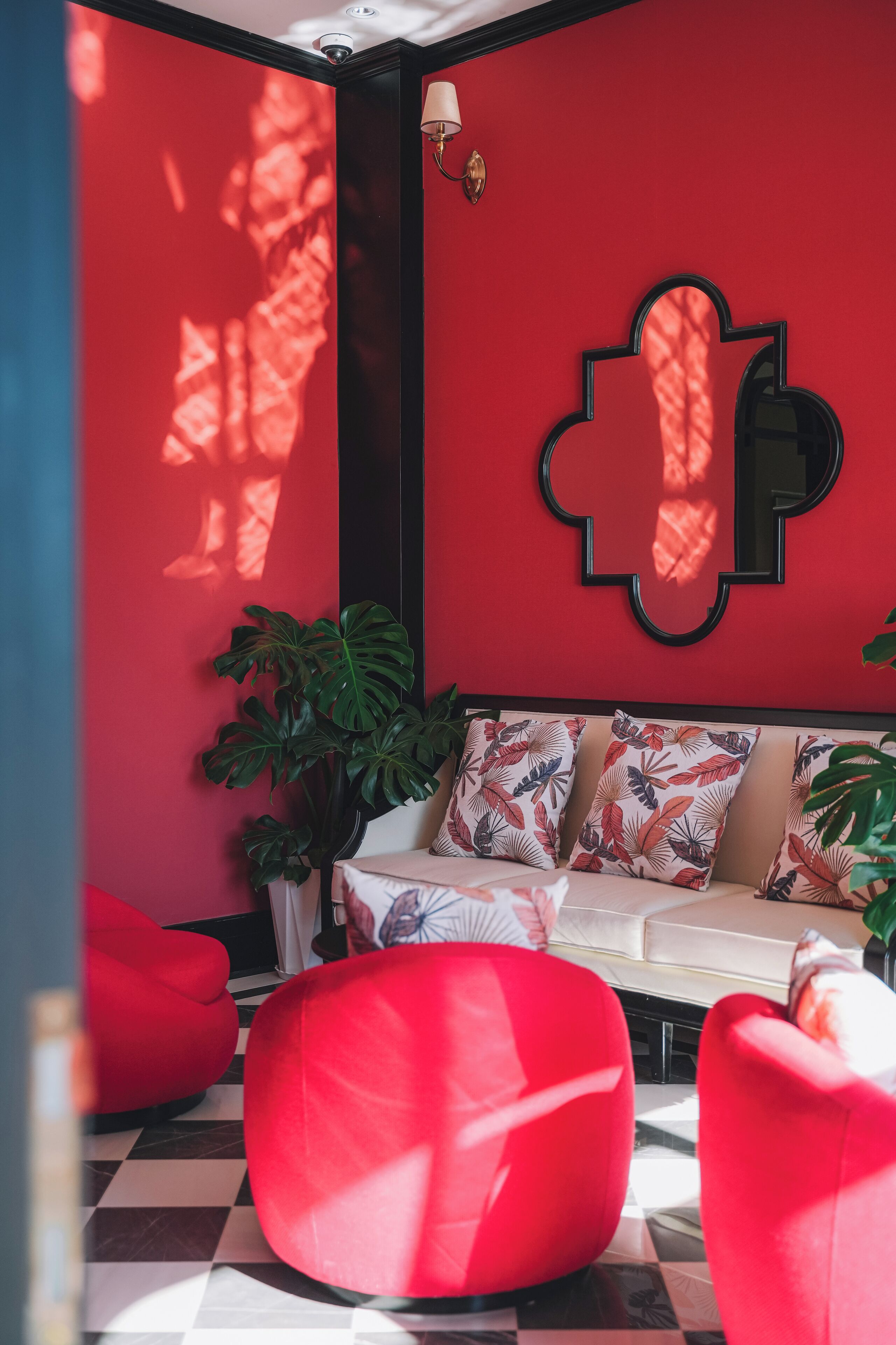 A room with a red wall, a white sofa with patterned cushions, a black-framed mirror, and red bean bag chairs.