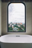 A bathroom with a bathtub and a window offering a view of a town.