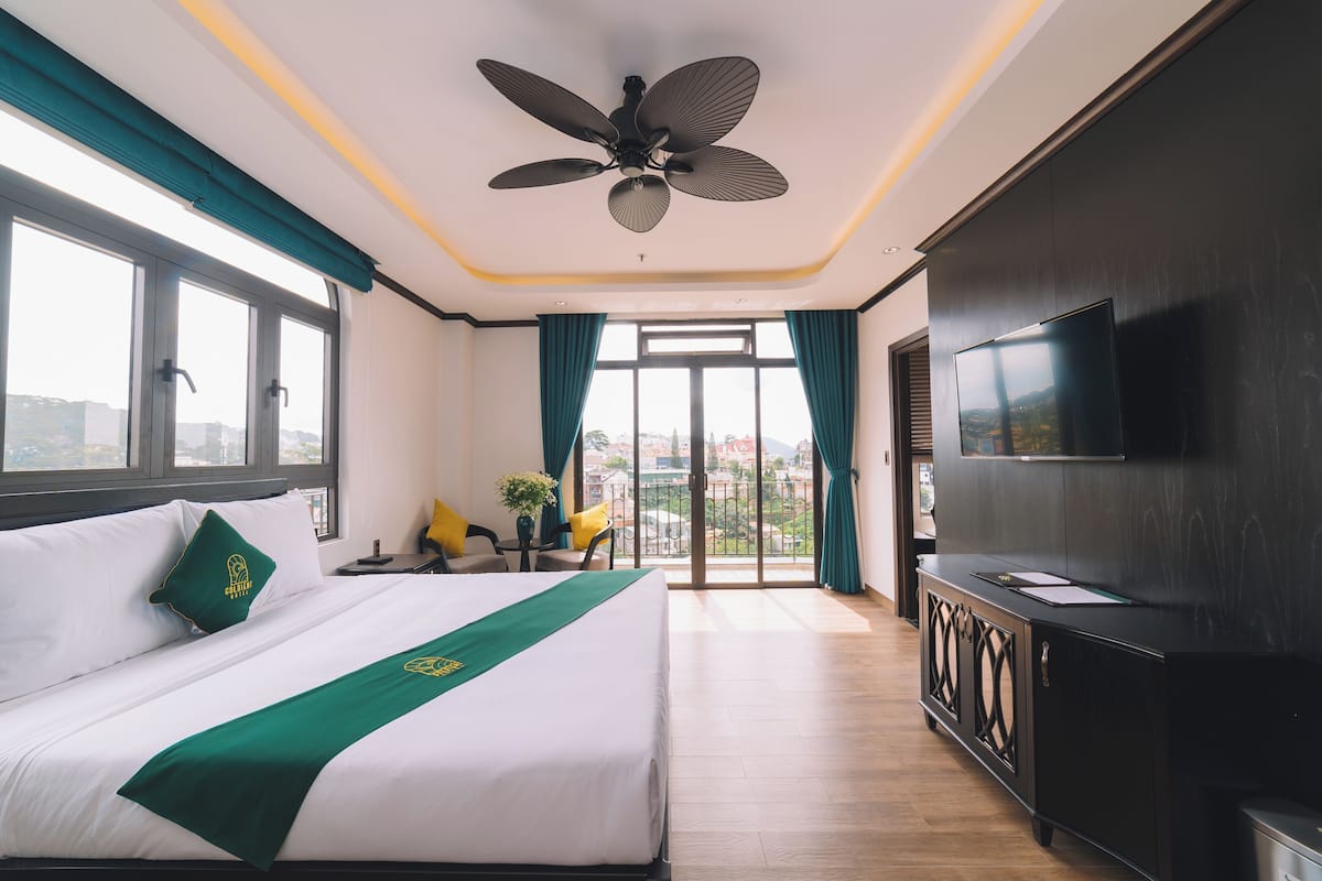A hotel room with a bed, a TV, a ceiling fan, a balcony with a view, and a desk with a chair.