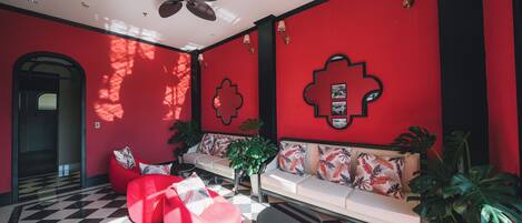 Un interior moderno con suelo de cuadros rojos y negros, un sofá con cojines estampados y un ventilador de techo.