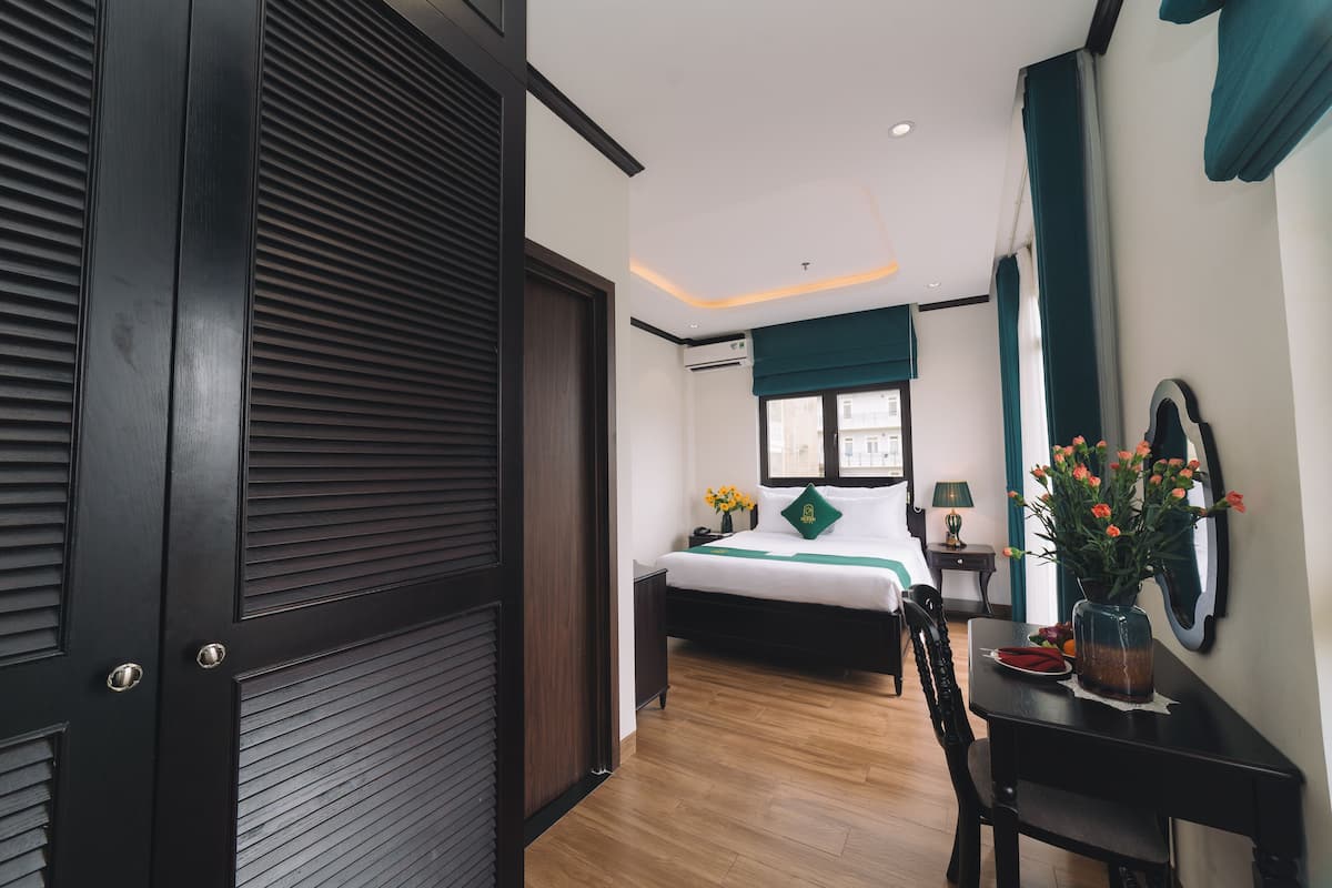 A hotel room with a bed, bedside table, and a desk with a vase of flowers.