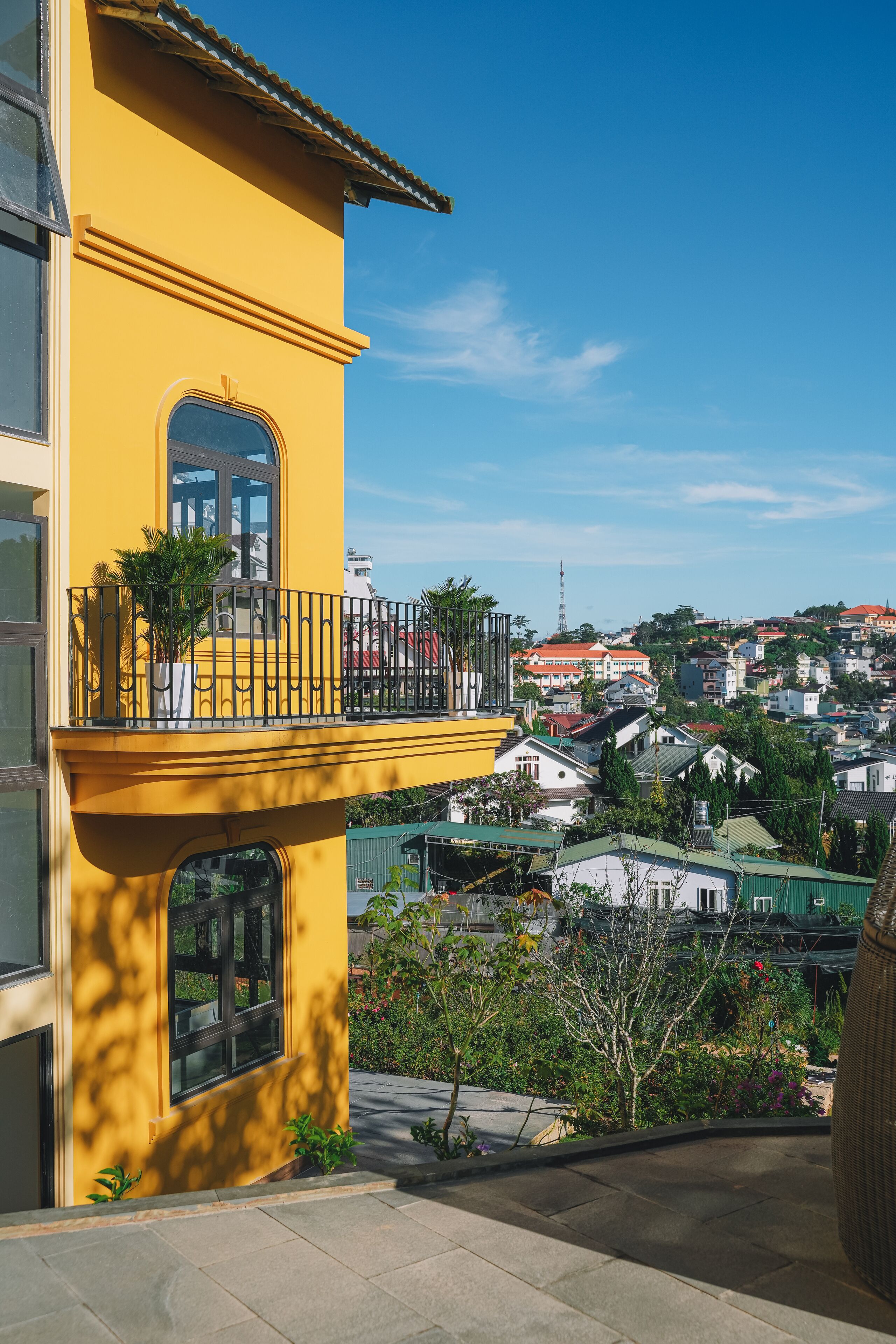 A yellow building with a balcony, a view of a residential area, and a clear blue sky.