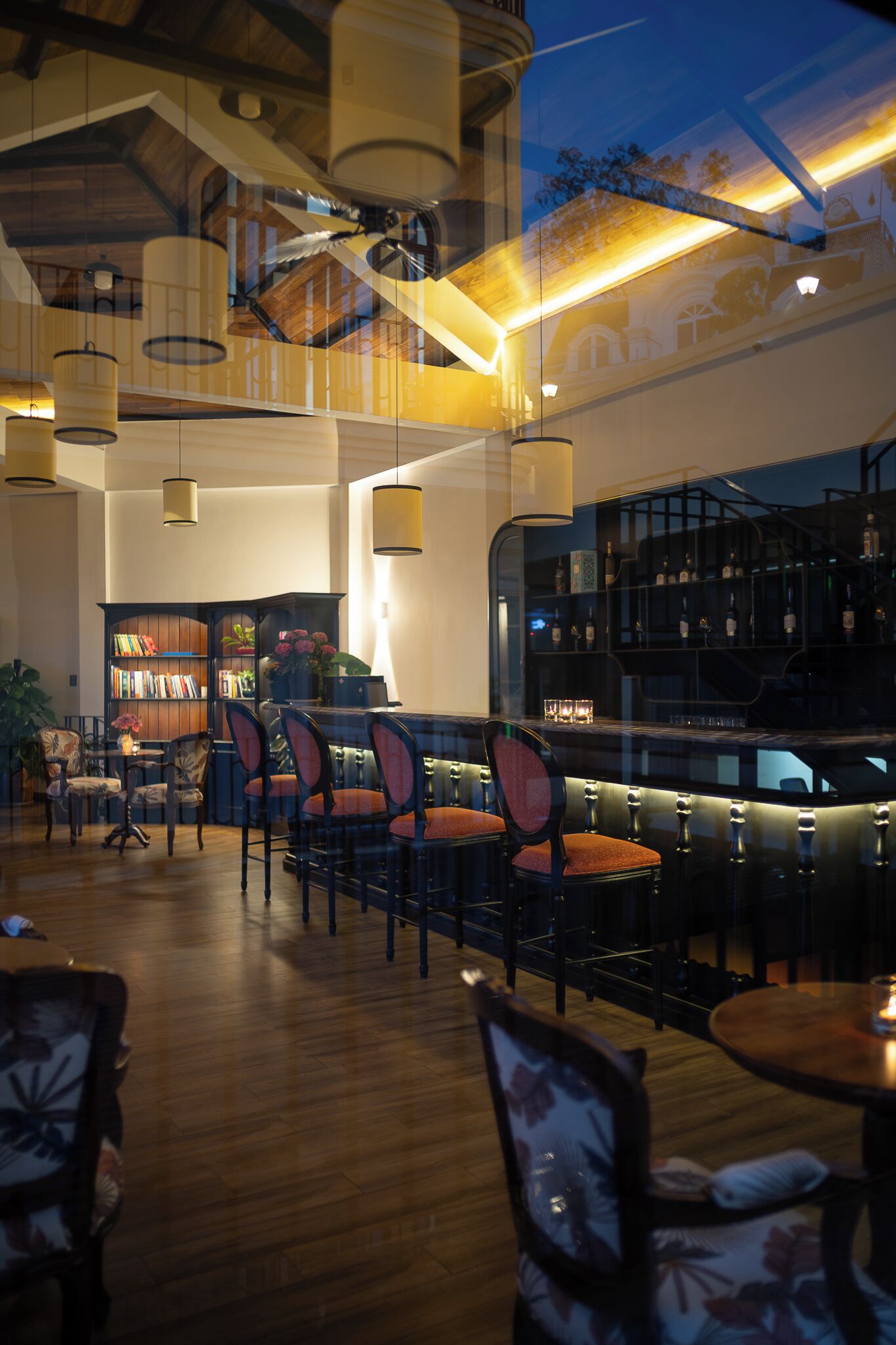 A bar area with wooden flooring, bar stools, and a bookshelf with books and decorative items.