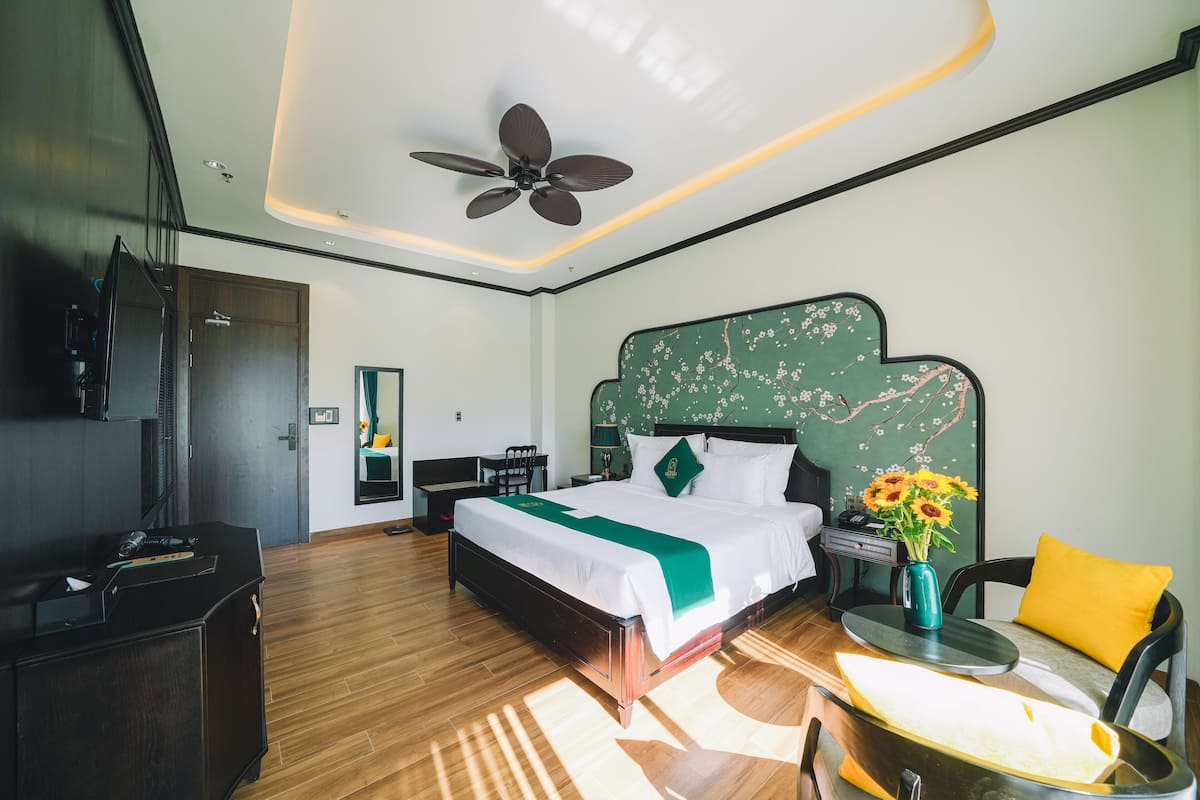 A modern hotel room with a large bed, a desk, a chair, a TV, and a ceiling fan.