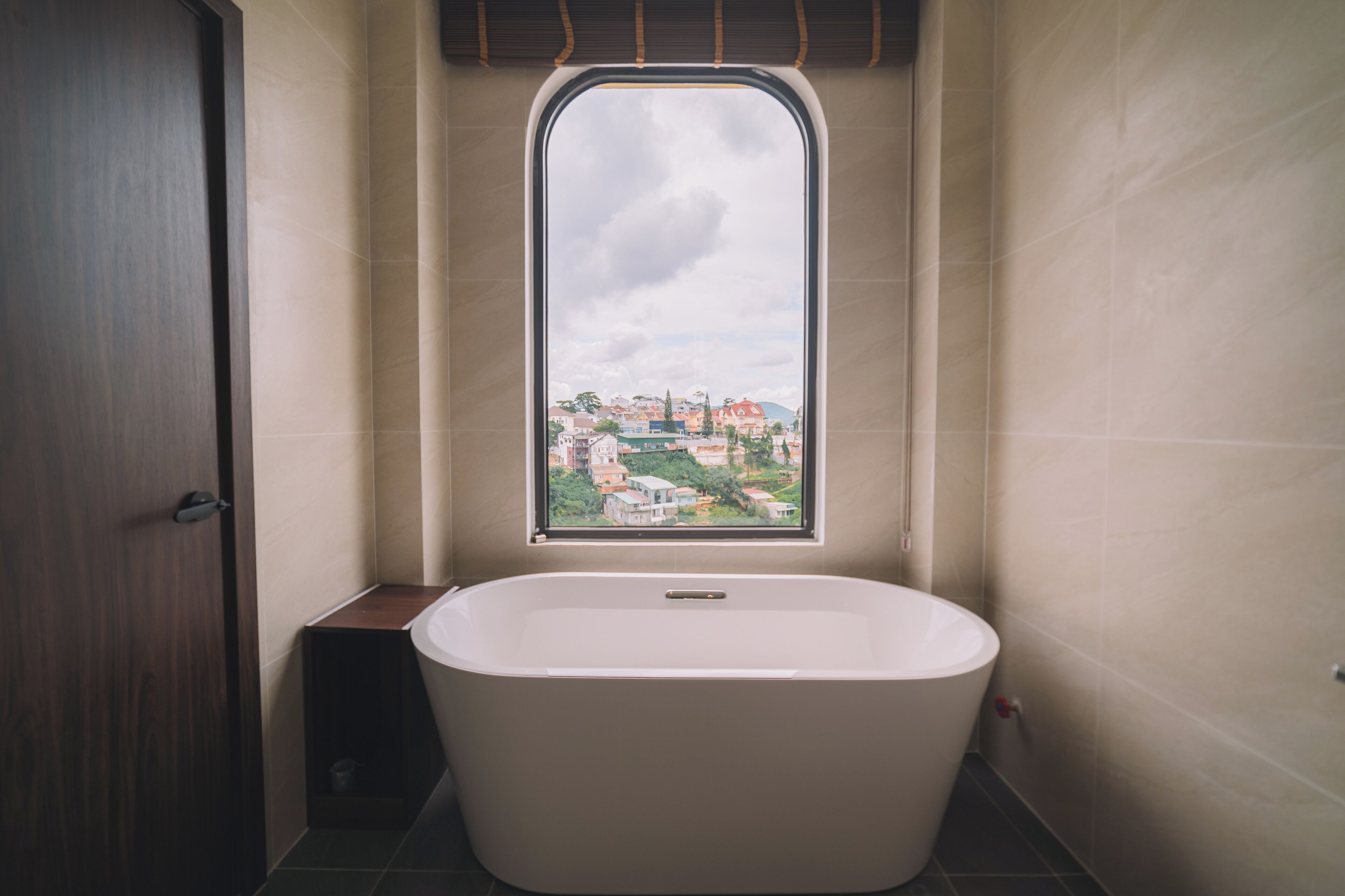 A bathroom with a bathtub, a window with a view of buildings, and a door.