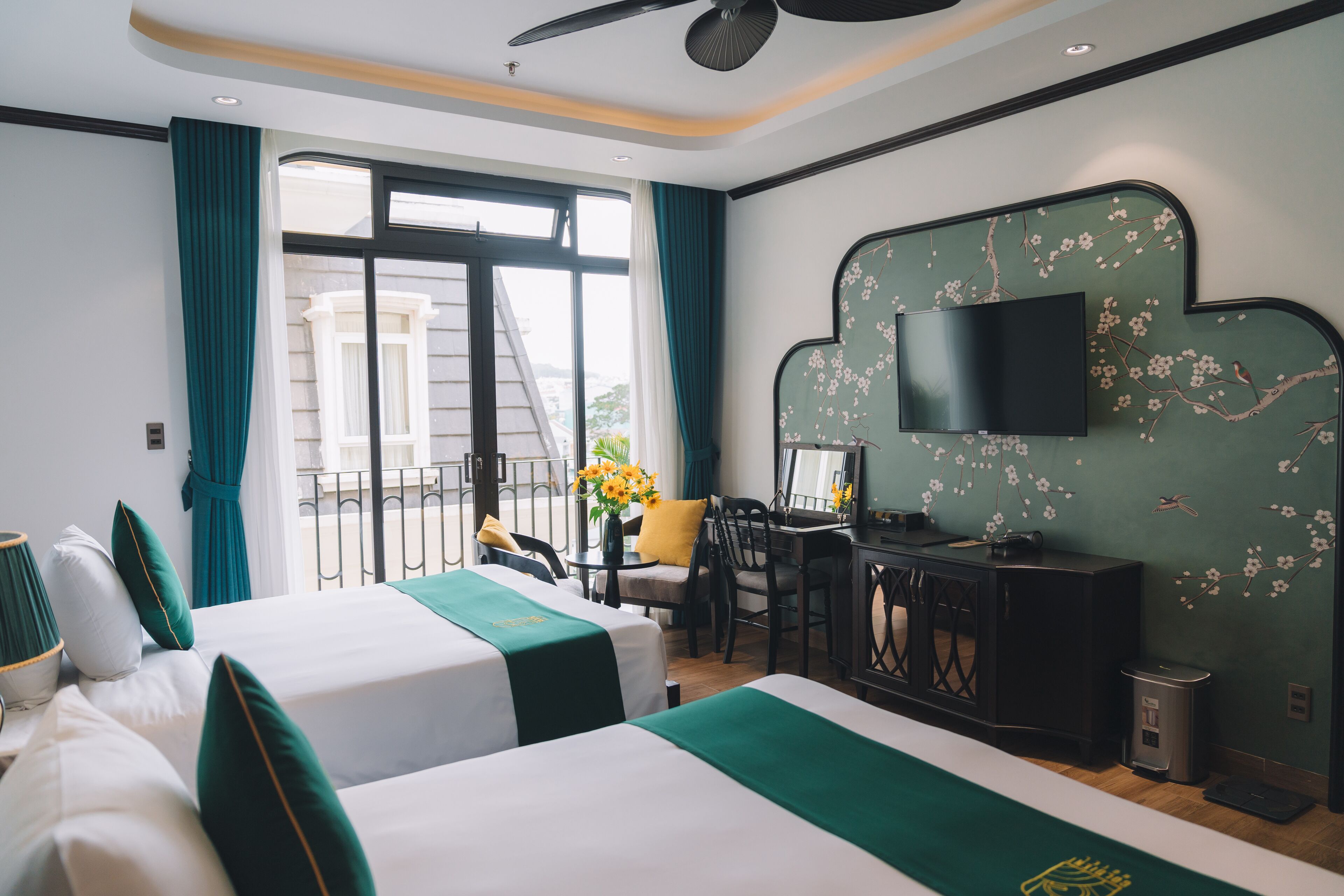 A hotel room with two beds, a desk, a chair, a TV, and a balcony with a view.