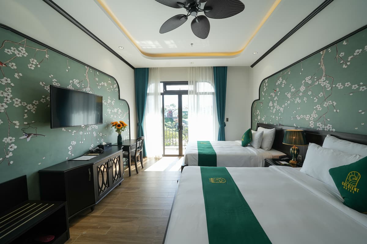 A hotel room with two beds, a TV, a desk with a chair, and a view of the outdoors.