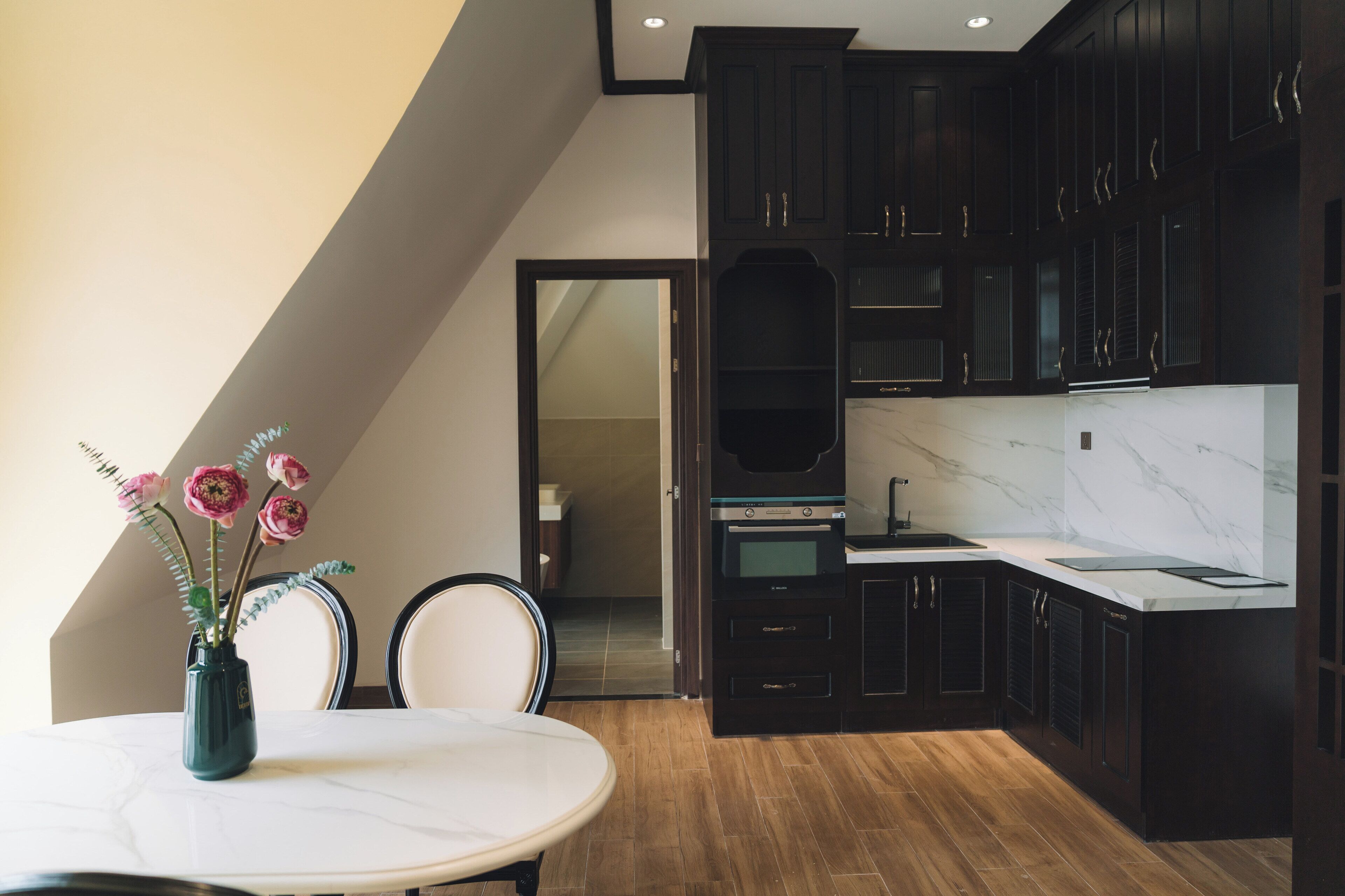 Una cocina moderna con armarios oscuros, encimera de mármol y un comedor con mesa y sillas.