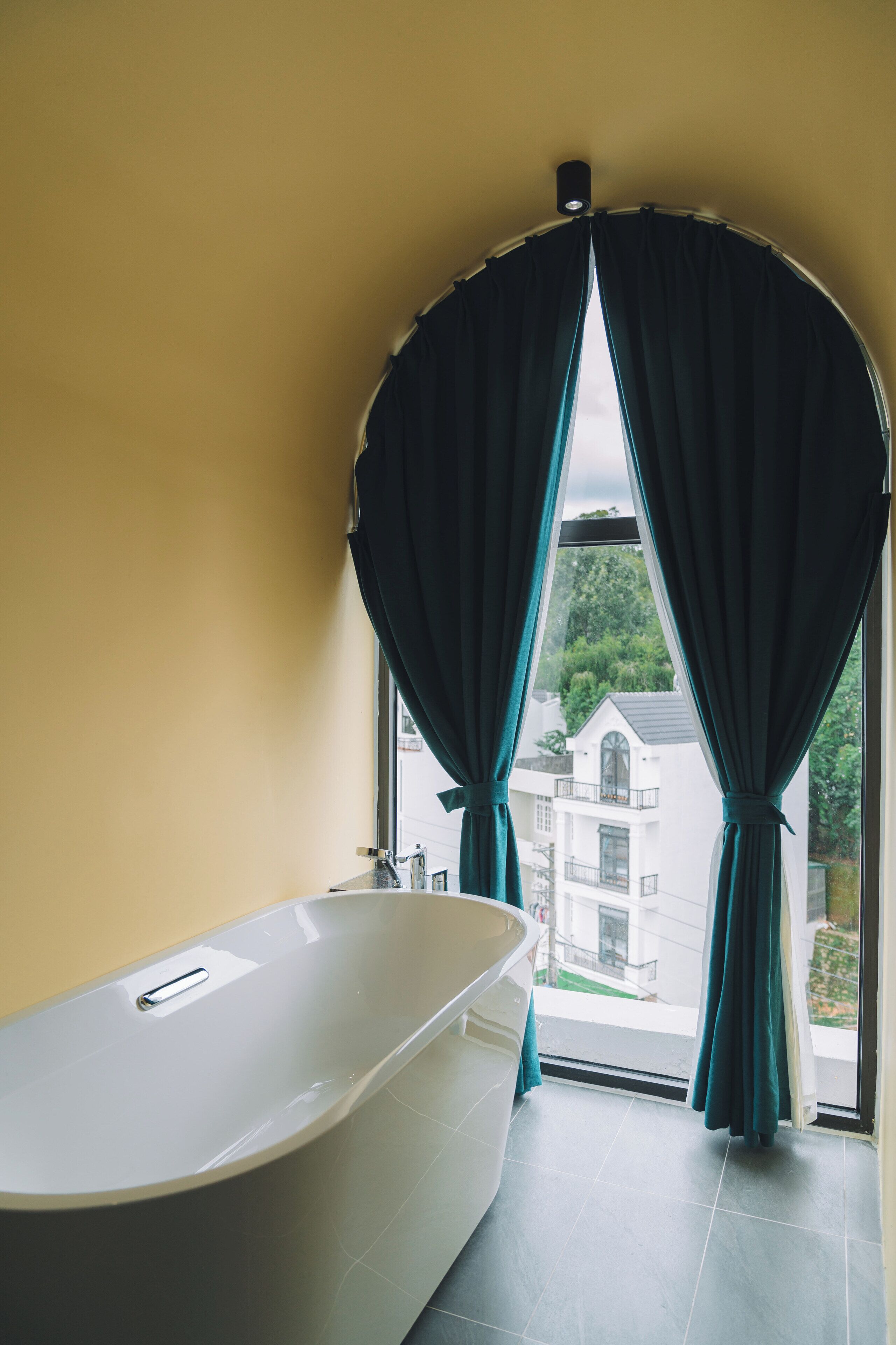 A bathroom with a freestanding bathtub, a window with curtains, and a view of a building outside.