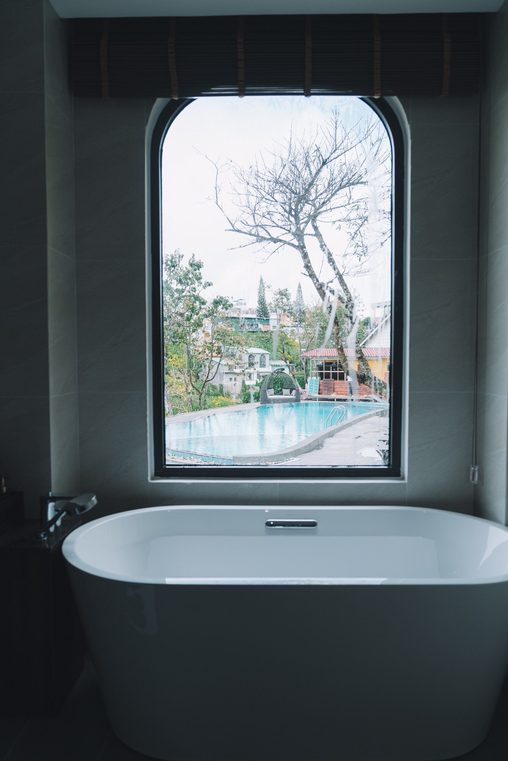Ein modernes Badezimmer mit freistehender Badewanne, einem Fenster mit Blick auf Pool und Bäume.