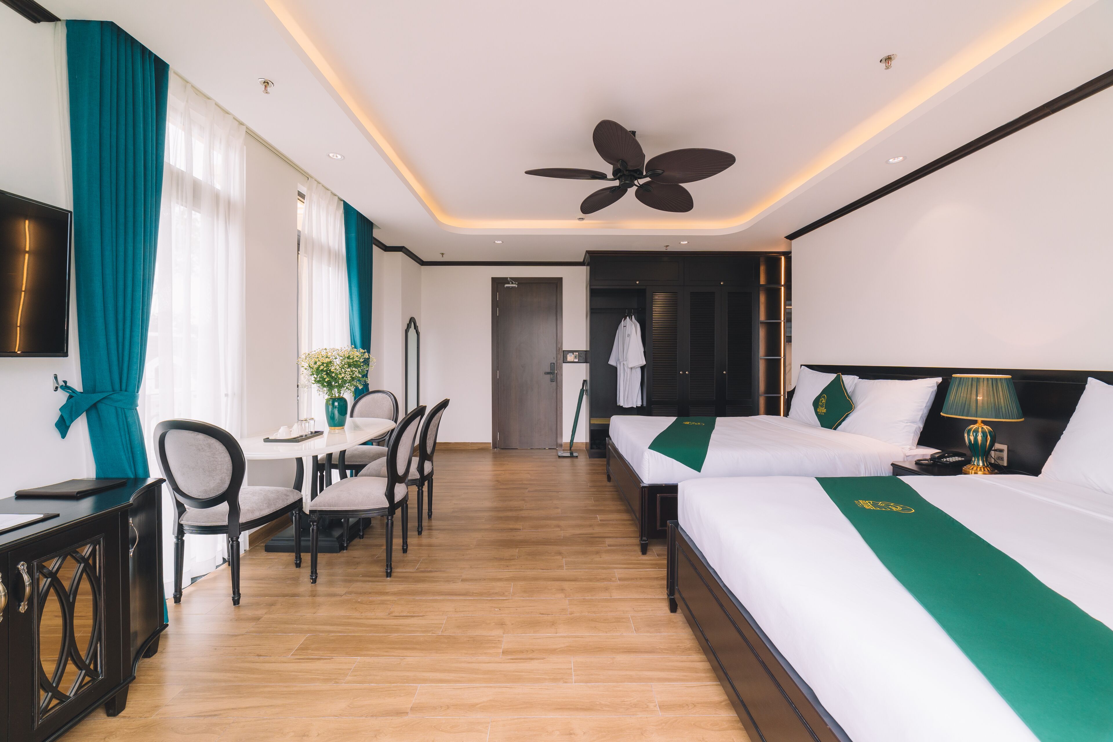 Une chambre d’hôtel équipée d’un lit, d’un bureau, d’une chaise, d’une télévision et d’un ventilateur de plafond.