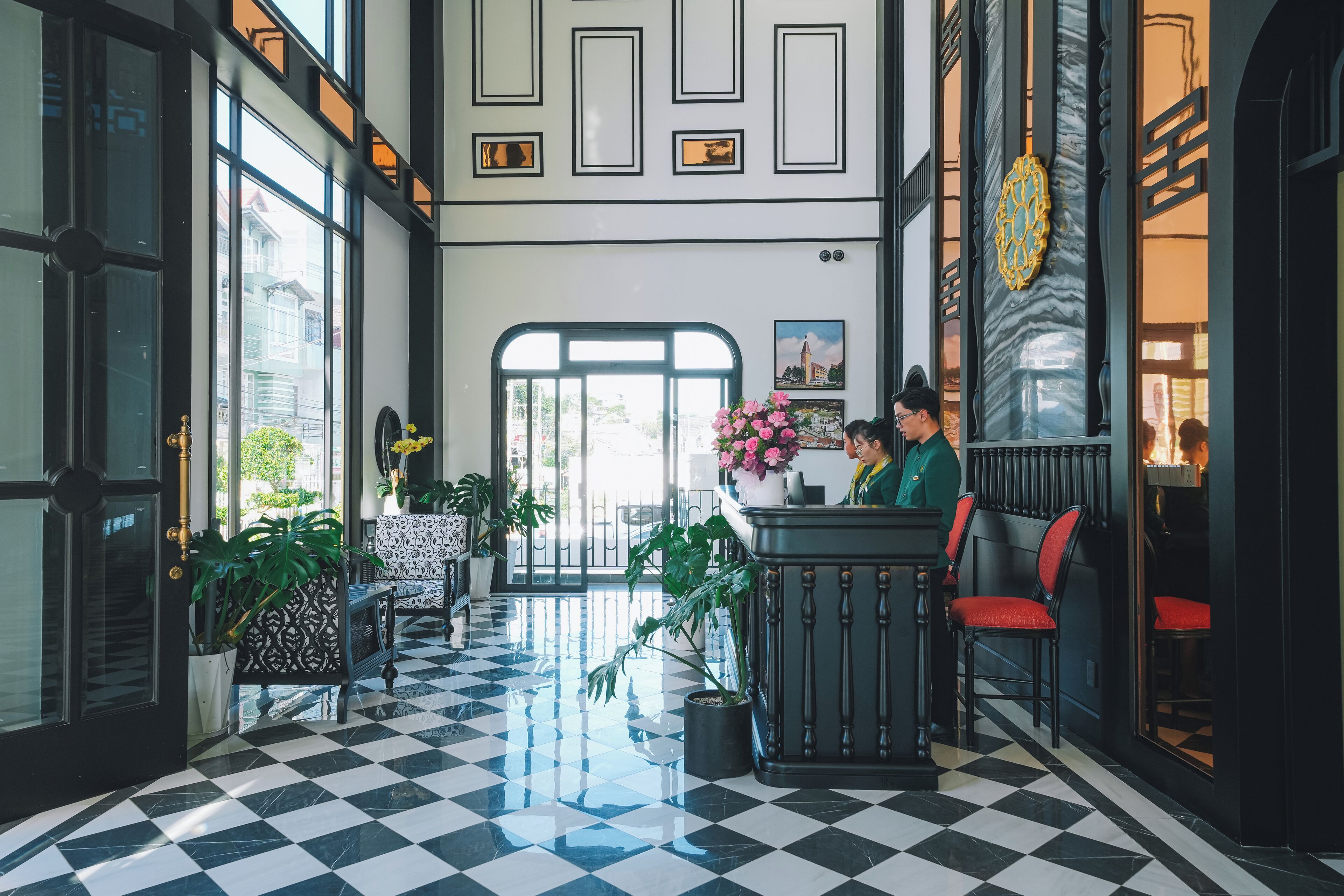 A lobby with a checkered floor, a reception desk, and potted plants.