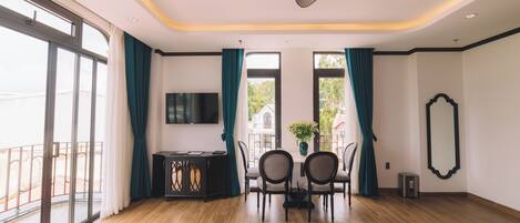 A hotel room with a large bed, a smaller bed, a dining table with chairs, a TV, and a balcony with a railing.