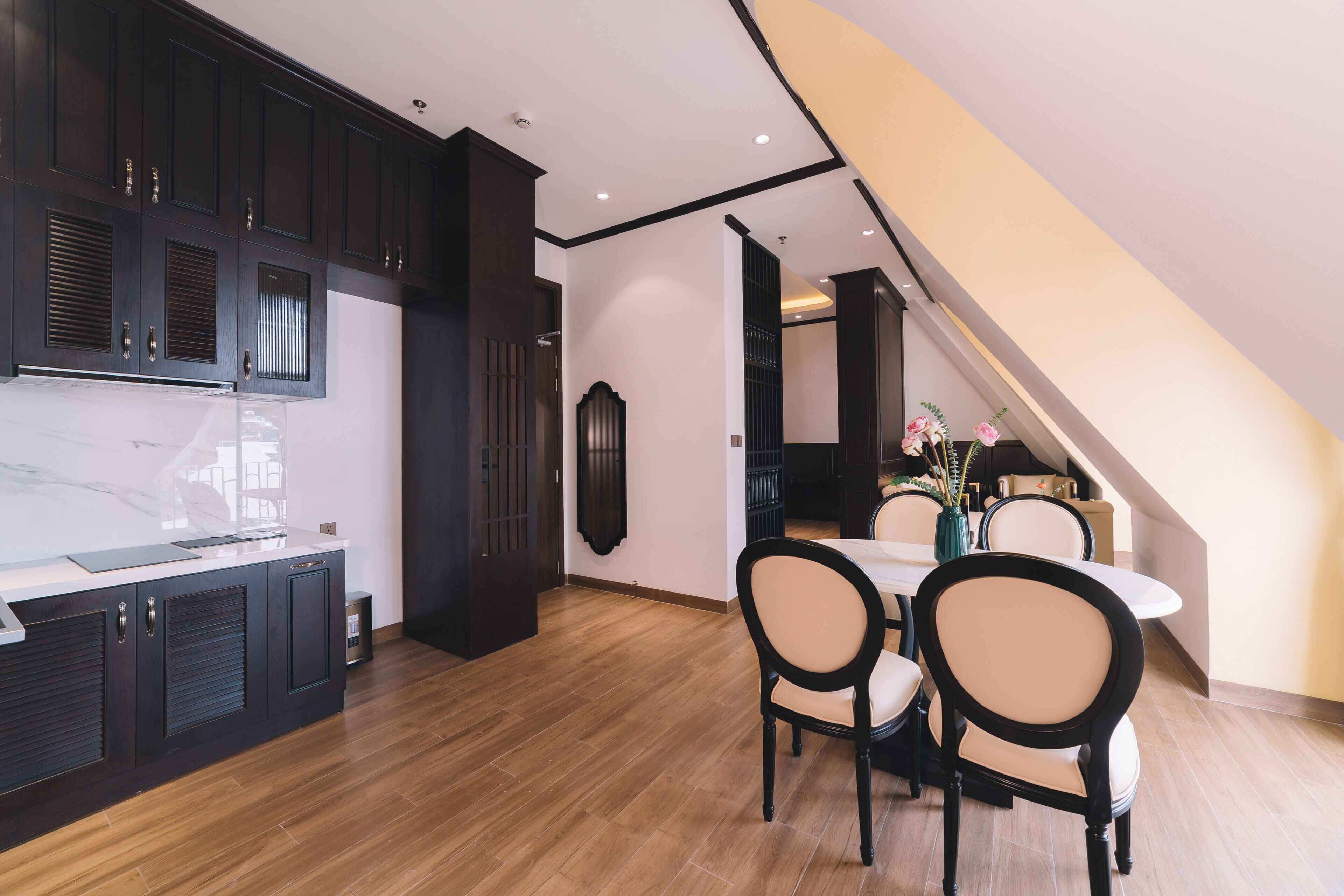 A modern kitchen with dark cabinetry, a marble countertop, and a dining area with a table and chairs.
