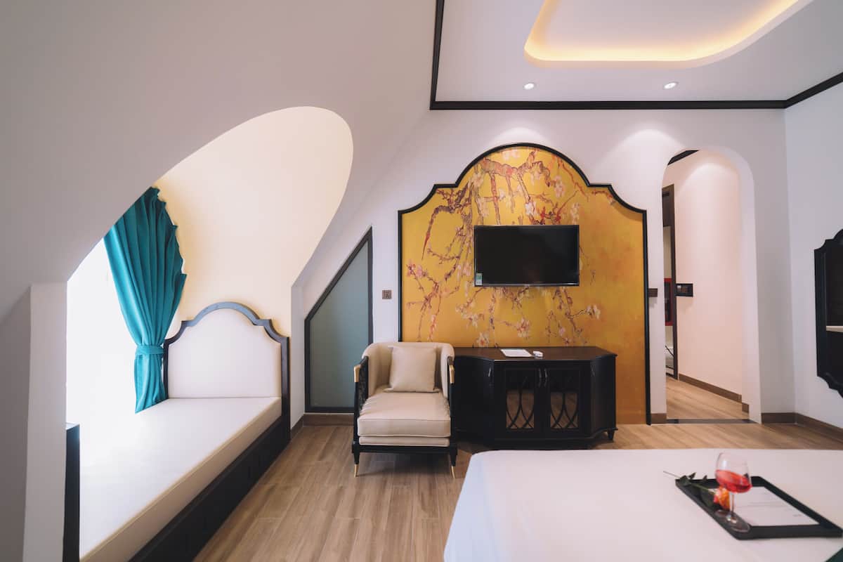 A modern hotel room with a sofa, armchair, and a flat-screen TV mounted on a decorative wall.