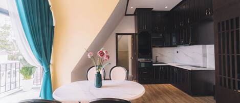 A modern kitchen with dark cabinets, a white countertop, and a dining area with a white table and chairs.