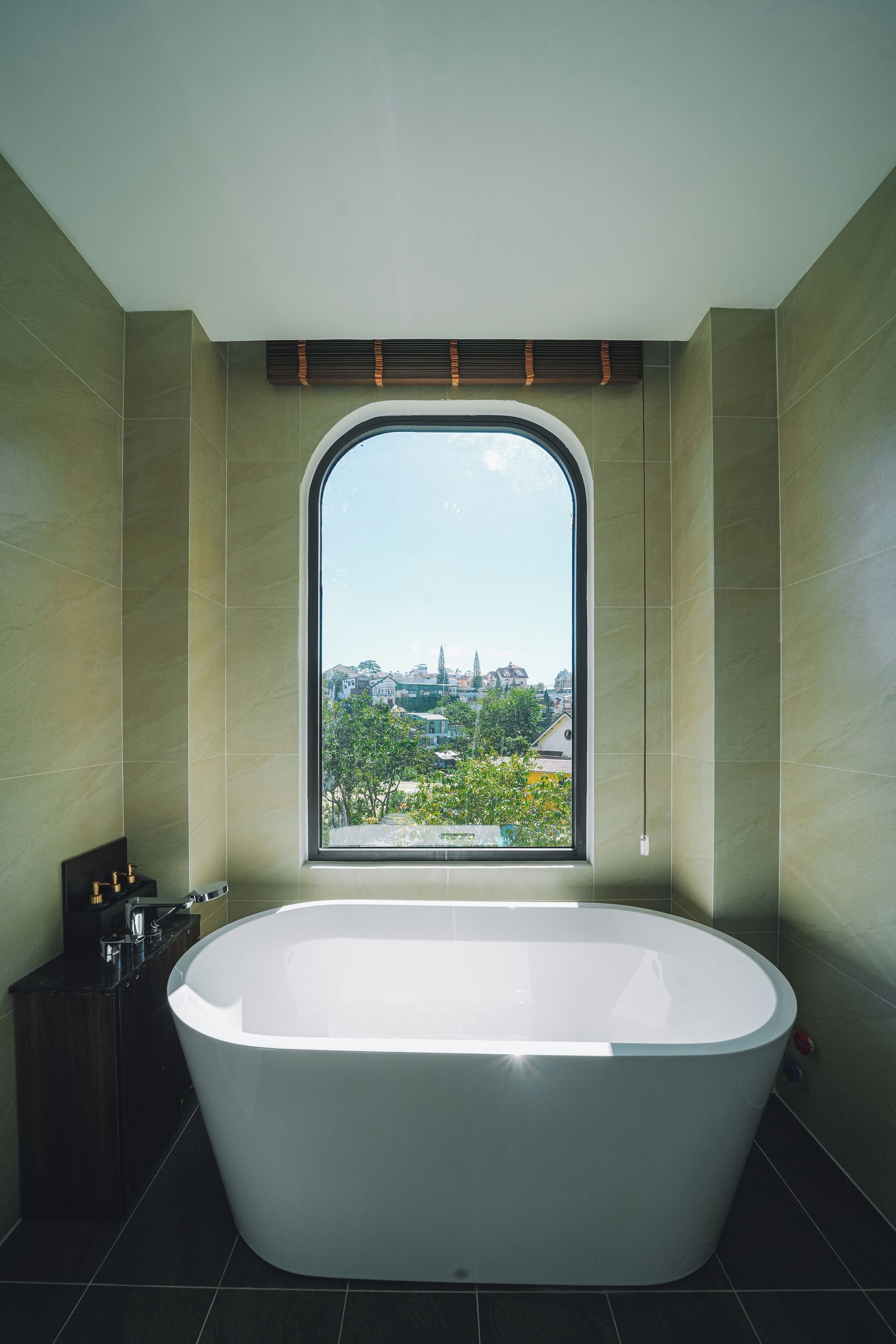 A modern bathroom with a freestanding bathtub, a window with a view of a cityscape, and a dark wooden cabinet.