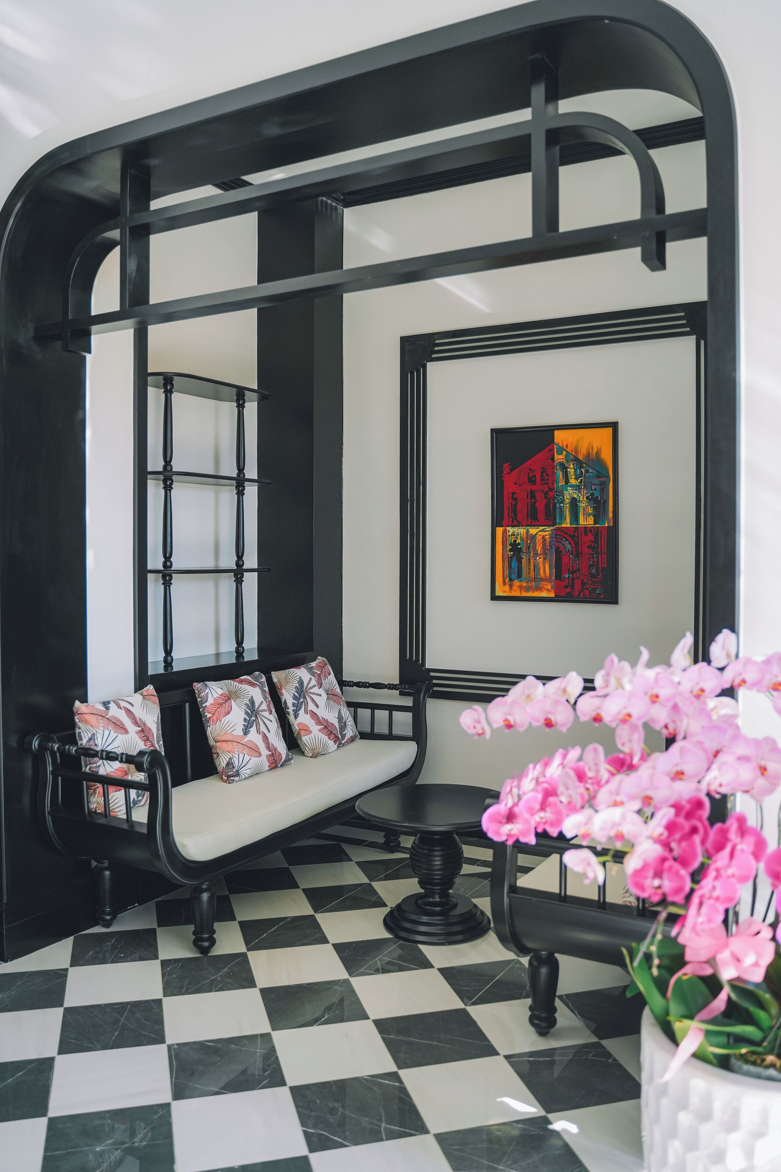 A black and white checkered floor, a black bench with floral cushions, a framed artwork, and pink orchids in a white pot.