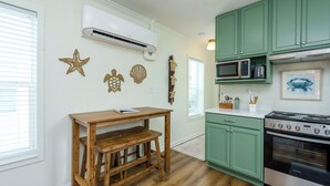 A kitchen with green cabinets, a wooden table, an air conditioner, and a stove. - Cozy cottage with easy access to beach & restaurants- Pet Friendly! (PASS CHRISTIN)