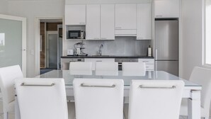 Una cucina moderna con mobili bianchi, un frigorifero in acciaio inossidabile, un forno a microonde e un lavello. È presente un tavolo da pranzo con quattro sedie bianche.