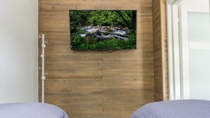 Una stanza con due letti, una parete in legno e un televisore che mostra una scena di natura.