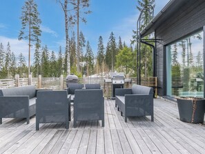 An outdoor deck with wicker furniture, a barbecue grill, and a view of a forest.