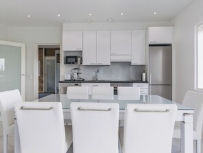 A modern kitchen with white cabinetry, a stainless steel refrigerator, and a glass dining table with white chairs.