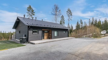En modern stuga i två våningar med ett sluttande tak, en veranda och en grusuppfart.