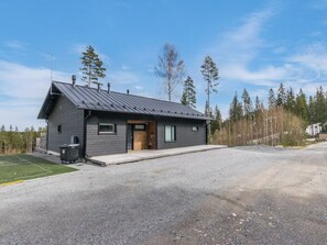 Moderni, kaksikerroksinen mökki, jossa on kalteva katto, kuisti ja sorapäällysteinen ajotie.