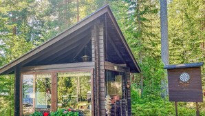 Uma cabana de madeira com fachada de vidro, rodeada por uma floresta densa.