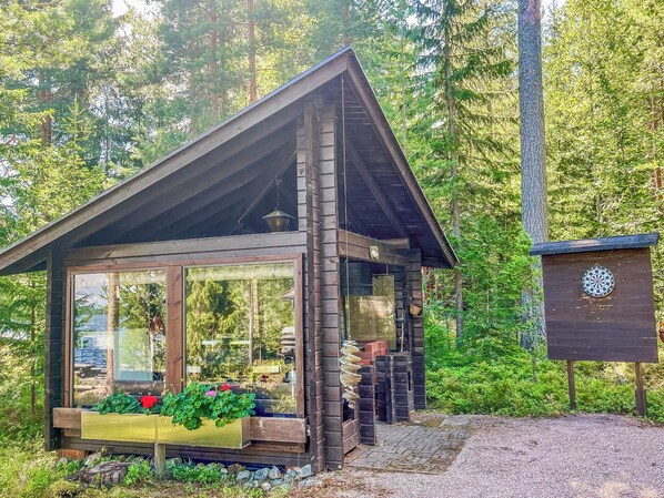 A cabin with a glass front, wooden deck, and a dartboard.