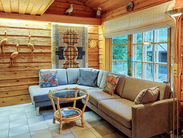 A cozy cabin interior with a sectional sofa, a small round table, and a large window. - Lauluranta by Interhome (Padasjoki)