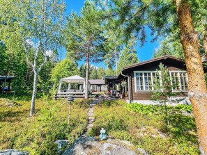 A cabin with a wooden exterior, a covered outdoor seating area, and a stone pathway leading to the entrance.