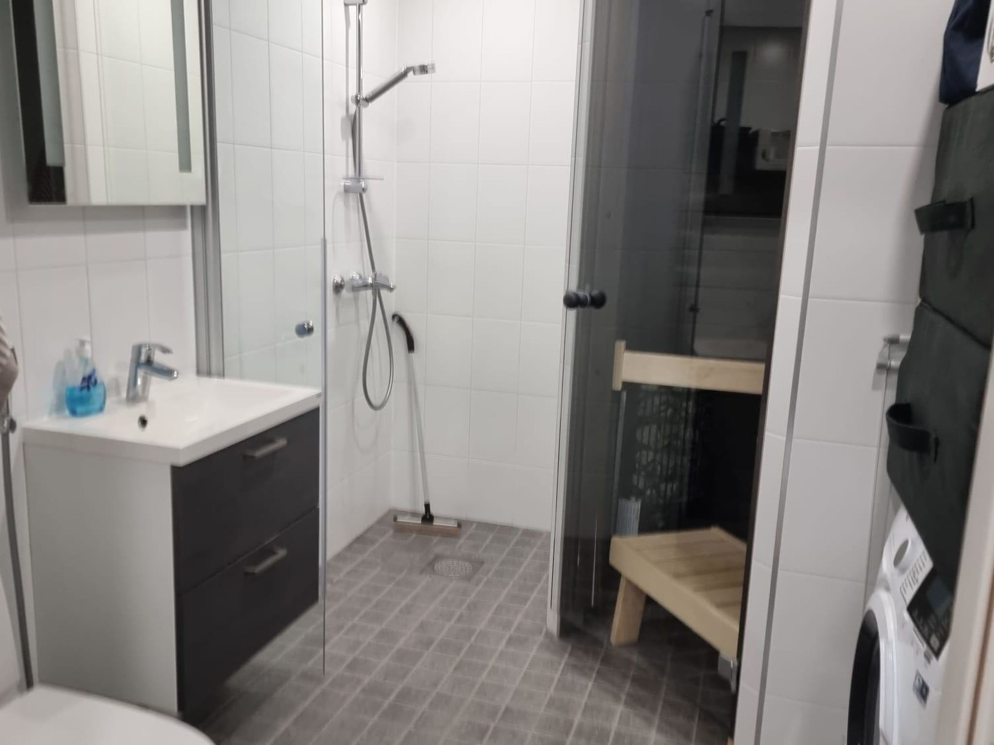 Ein Badezimmer mit einem weißen Waschbecken, einem Spiegel, einer Dusche mit Glastür und einer hölzernen Sitzbank.
