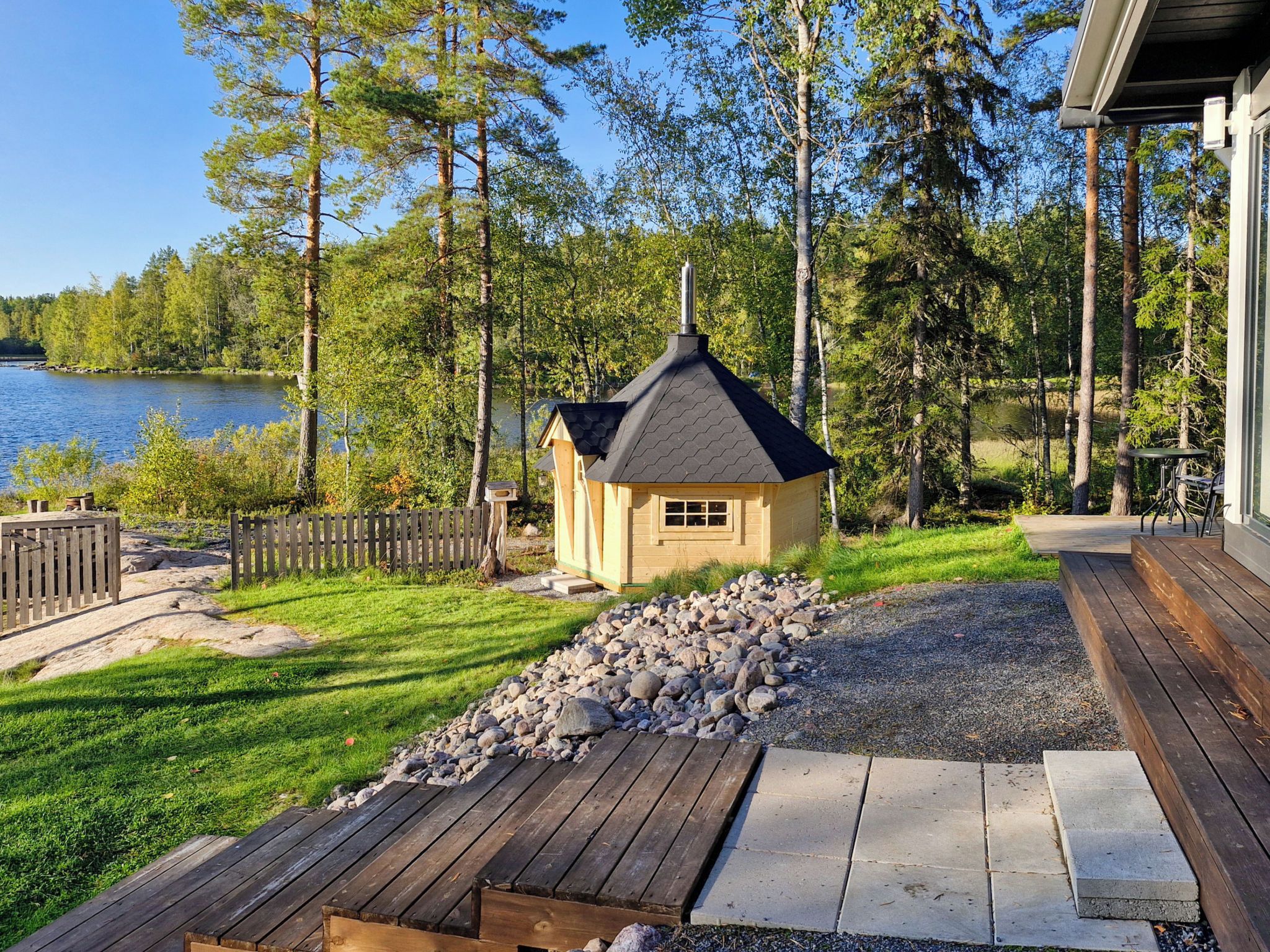 A cabin with a deck, surrounded by a natural landscape and a lake.