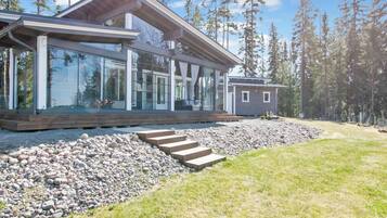 A modern house with large glass windows, a wooden deck, and a stone pathway leading to the entrance.