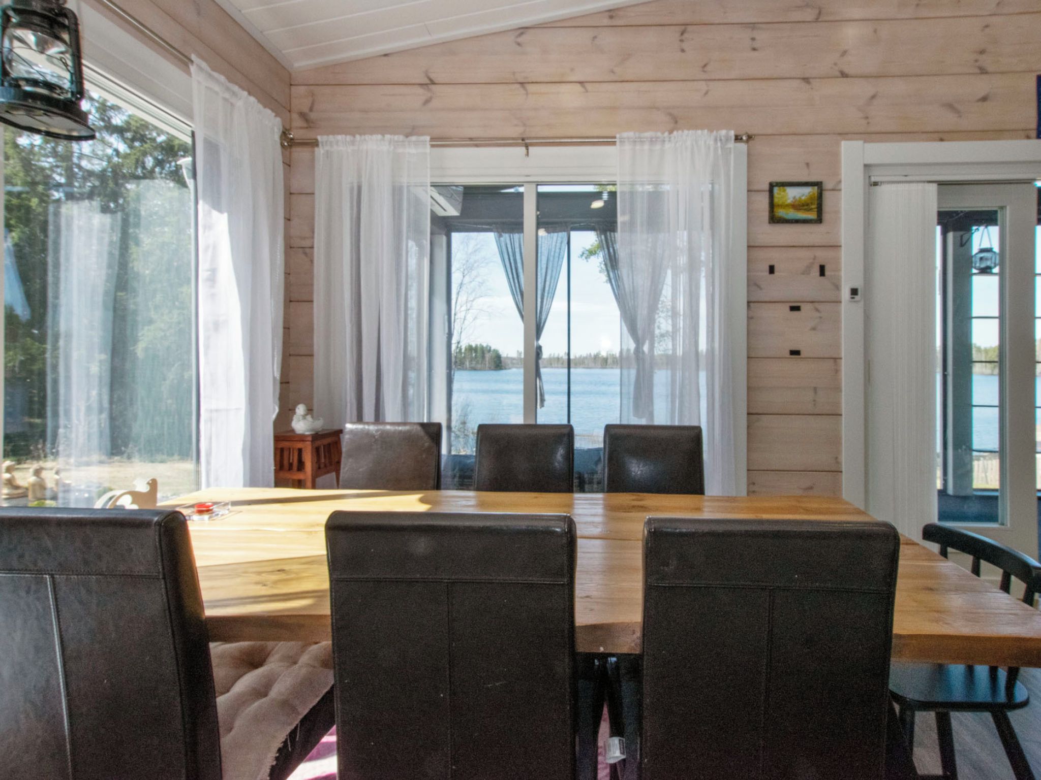 Un espace repas avec une table et des chaises en bois, de grandes fenêtres avec des rideaux et une vue sur une étendue d’eau.