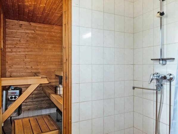 A wooden cabin bathroom with a shower, a bench, and a small table with a kettle.