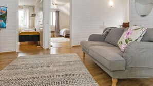 Una habitació àmplia amb un sofà gris, una catifes amb disseny i un llit amb col·cha groga i negra.
